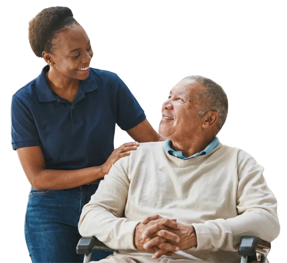 Smiling female caregiver with a hand on the shoulder of an elderly man sitting in a wheelchair.