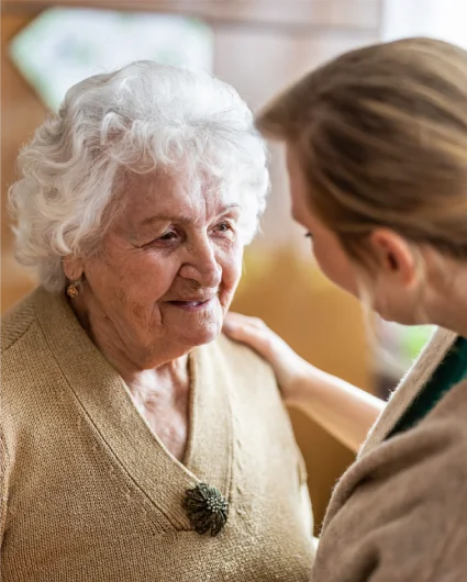 Young woman gently placing a comforting hand on the shoulder of an elderly woman during a conversation.