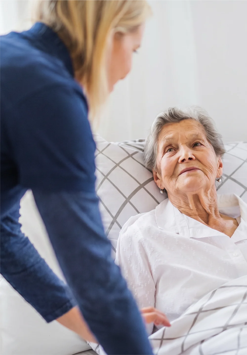 Caregiver attending to an elderly woman lying in bed.