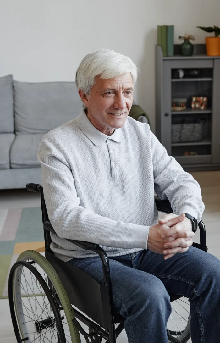 Smiling elderly man sitting in a wheelchair inside a cozy living room.