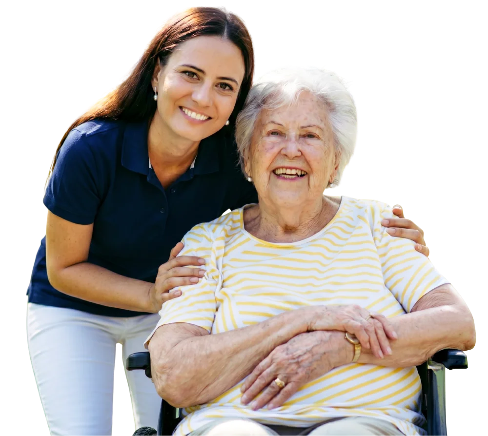 Caregiver smiles beside elderly woman in a wheelchair.