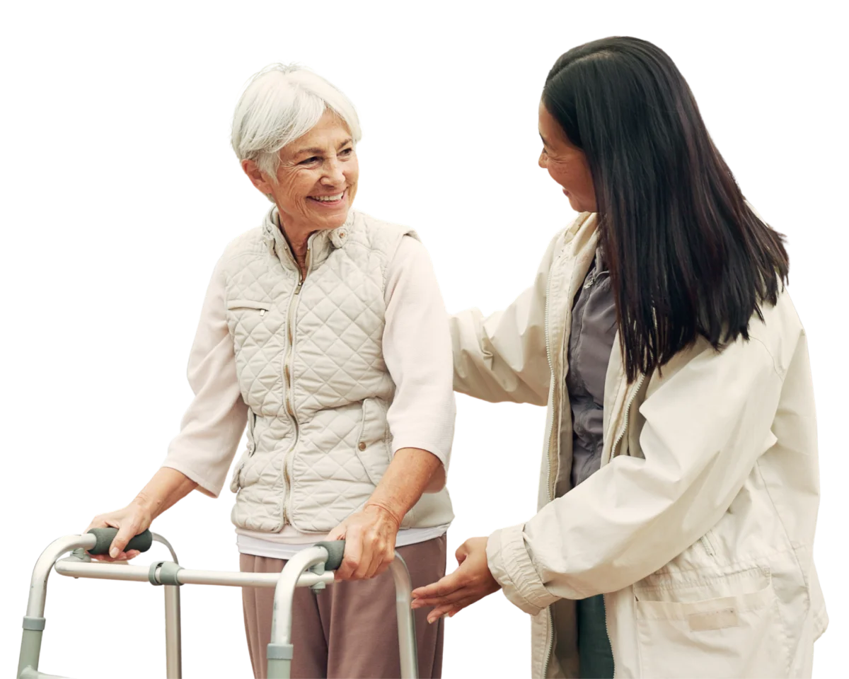 Elderly woman using a walker smiles while a caregiver supports her.
